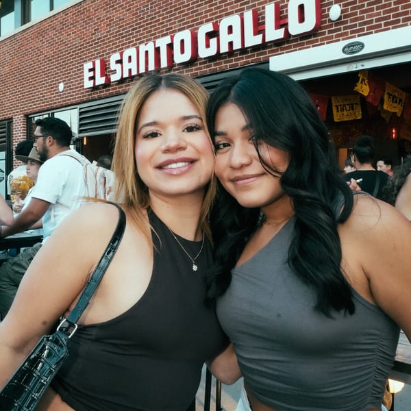 Two smiling women posing in front of the El Santo Gallo Taqueria sign.