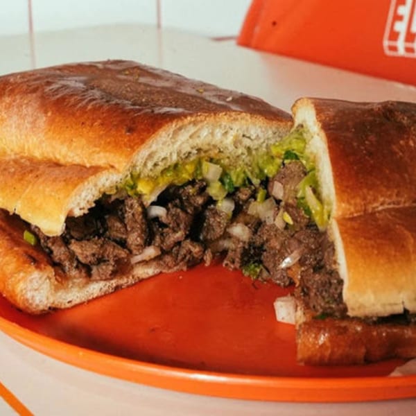 A large El Santo Gallo Taqueria torta, cut in half, filled with meat, onions, and green sauce.