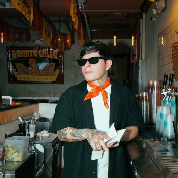 Bartender with tattoos and sunglasses holding paper, standing at the bar of El Santo Gallo Taqueria.