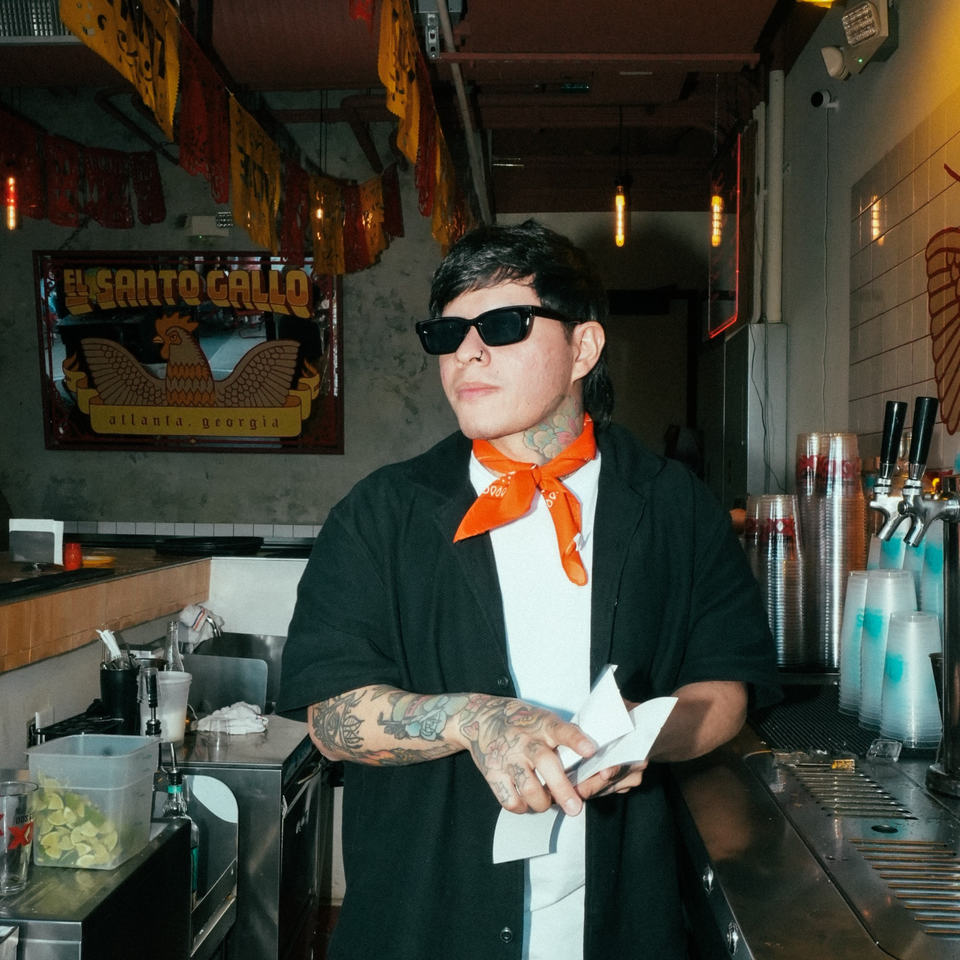 Bartender with tattoos and sunglasses holding paper, standing at the bar of El Santo Gallo Taqueria.