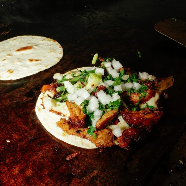 El Santo Gallo Taqueria's taco with meat, onions, and cilantro on a griddle with a tortilla.
