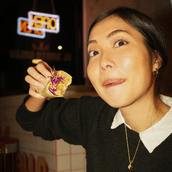 A woman holding a Mexican taco, looking at the camera with her tongue out.