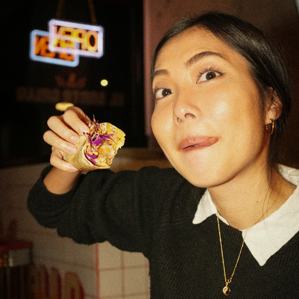 A woman holding a Mexican taco, looking at the camera with her tongue out.