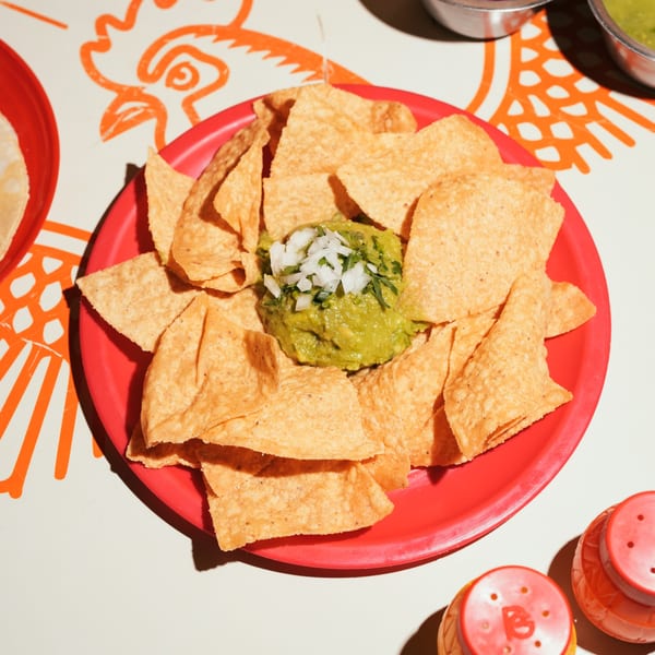 Guacamole topped with diced onions and cilantro, surrounded by tortilla chips on a red plate.